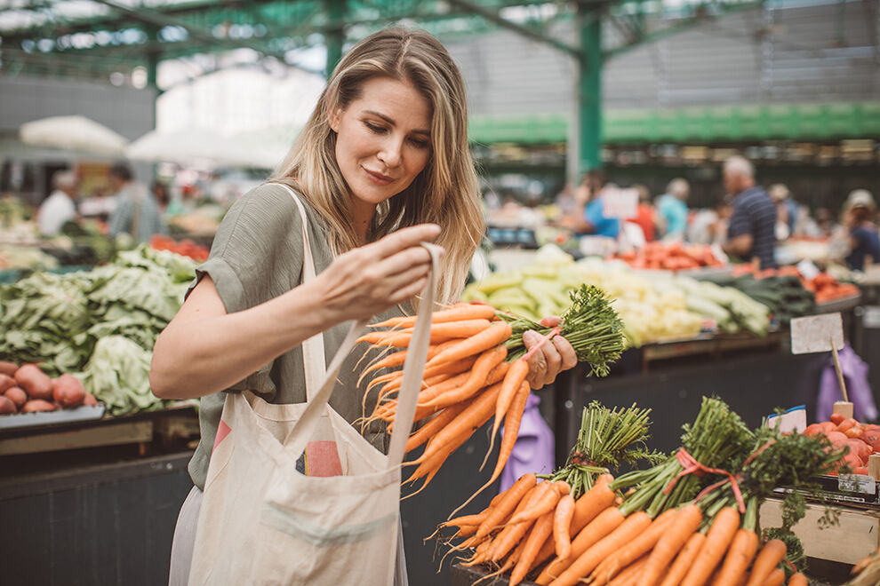 Frau kauft auf einem Markt Gemüse ein
