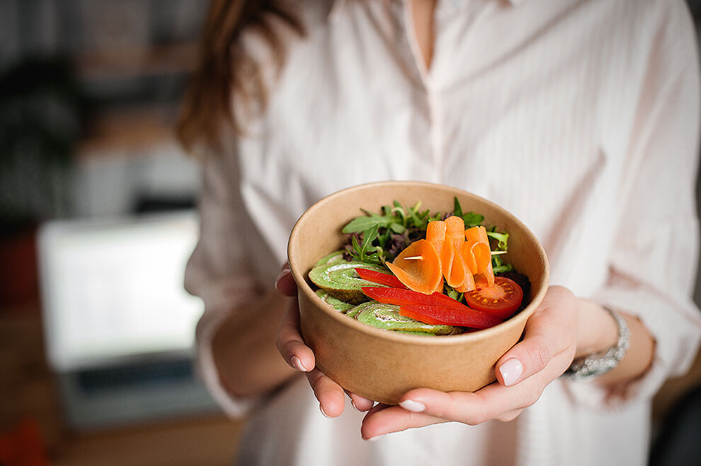 Gesunde Ernährung: Eine Frau hält eine Pappchale mit Salat und gesundem Essen.