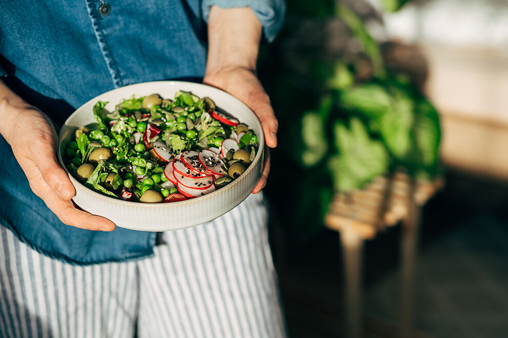 Hände mit veganem Salat aus gebackenem Gemüse, Avocado, Tofu und Buchweizen, Buddha-Bowl, Draufsicht. Pflanzliches Lebensmittelkonzept.