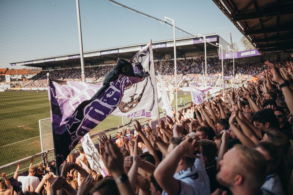 Eine Foto von jubelnden VfL Fans beim Zuschauen eines Spiels.