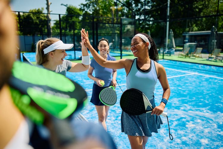 Eine Gruppe Frauen geben sich high five nach einem Padelspiel.