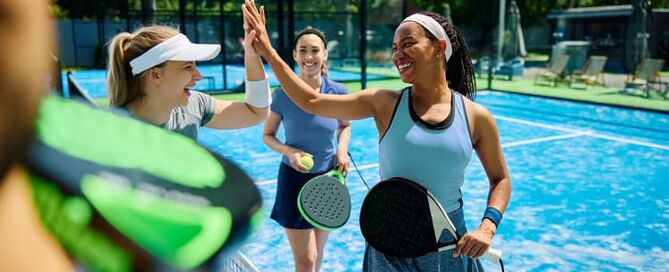 Eine Gruppe Frauen geben sich high five nach einem Padelspiel.