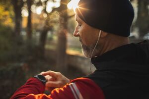 Ein Mann steht im Wald mit Kopfhörern in den Ohren und schaut auf seine Smart Watch.