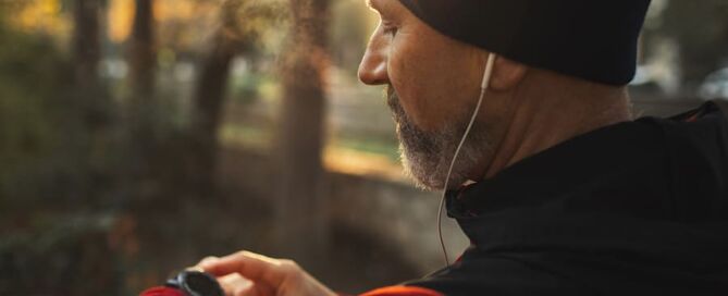 Ein Mann steht im Wald mit Kopfhörern in den Ohren und schaut auf seine Smart Watch.