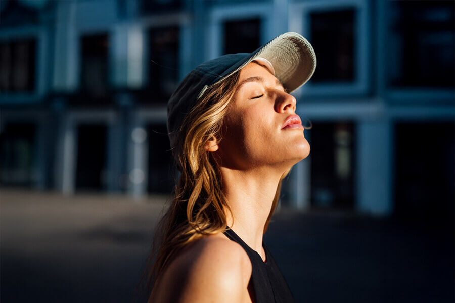 Eine Frau schließt die Augen und genießt Sonnenstrahlen auf ihrem Gesicht.