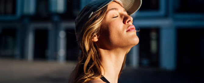 Eine Frau schließt die Augen und genießt Sonnenstrahlen auf ihrem Gesicht.