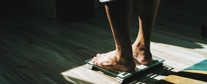 Das morgendliche Sonnenlicht erhellt eine Person die gerade auf die Waage steigt.