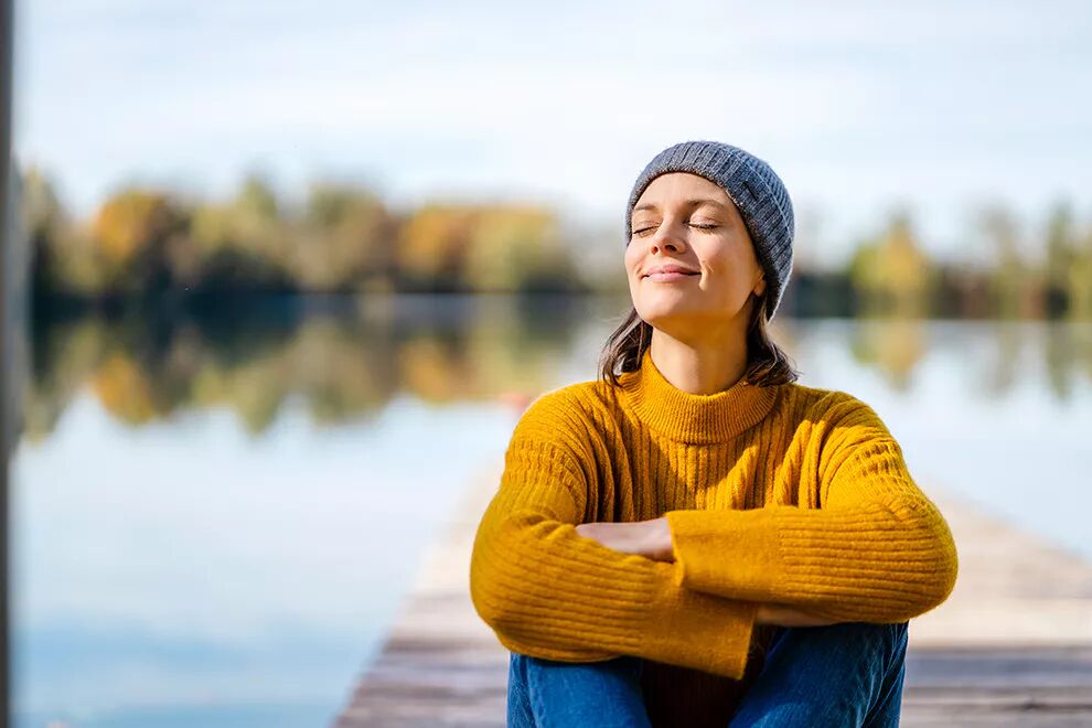Eine Frau sitzt auf einem Steg am See in der Sonne.
