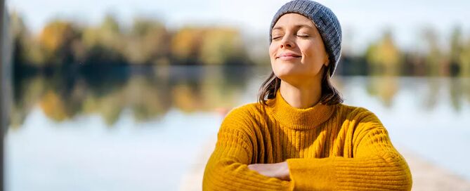 Eine Frau sitzt auf einem Steg am See in der Sonne.