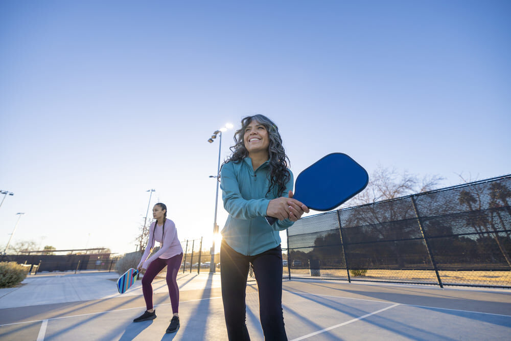 pickleball-1 Zwei Frauen warten mit gehobenen Schlägern auf den nächsten Schlag des anderen Teams.